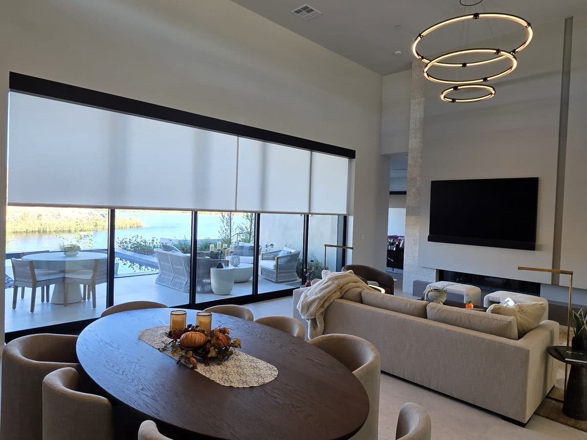 Motorized roller shades lowered partway over the great room's glass wall, with the patio and lake below them