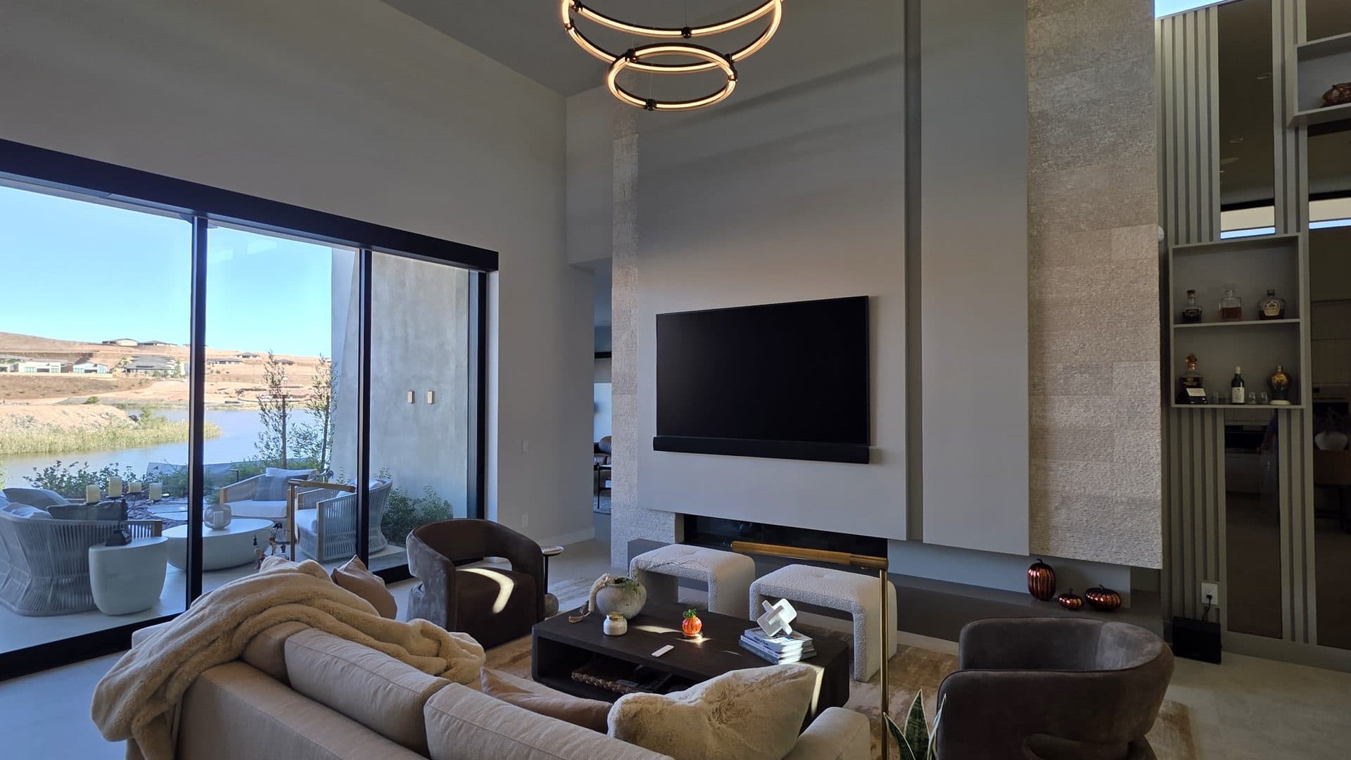 Great room with a wall-mounted Samsung Frame TV and soundbar, a ring chandelier and floor-to-ceiling glass looking out to the lake