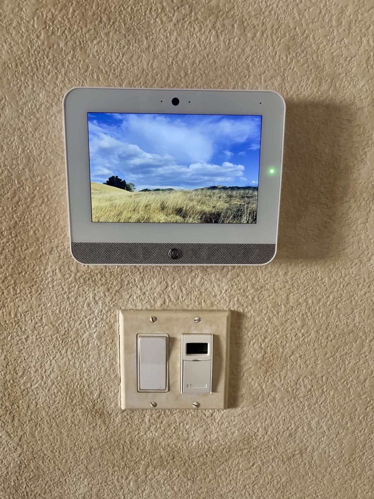 Qolsys IQ Panel 5 alarm touch screen mounted on a textured wall above a light switch